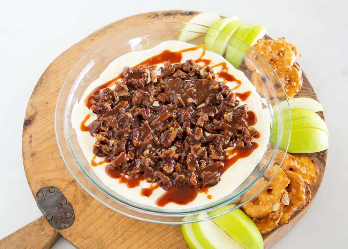 Pecan pie dip topped with chopped pecans and caramel, served with apple slices and pretzels.