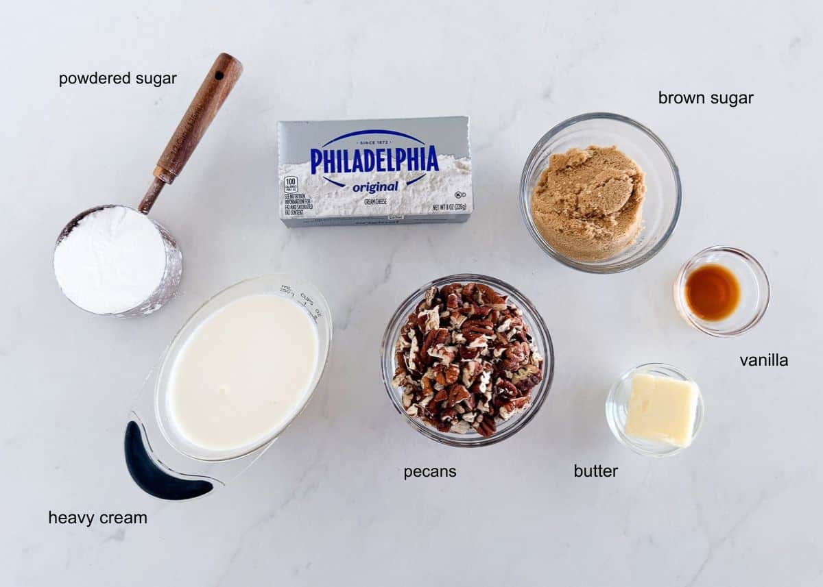 Ingredients for pecan pie dip arranged on a counter, including cream cheese, powdered sugar, brown sugar, pecans, butter, cream and vanilla.