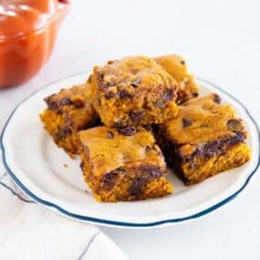 Pumpkin chocolate chip cake squares stacked on a white plate with melted chocolate chips throughout.