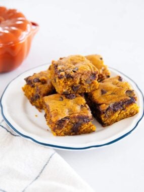 Pumpkin chocolate chip cake squares stacked on a white plate with melted chocolate chips throughout.