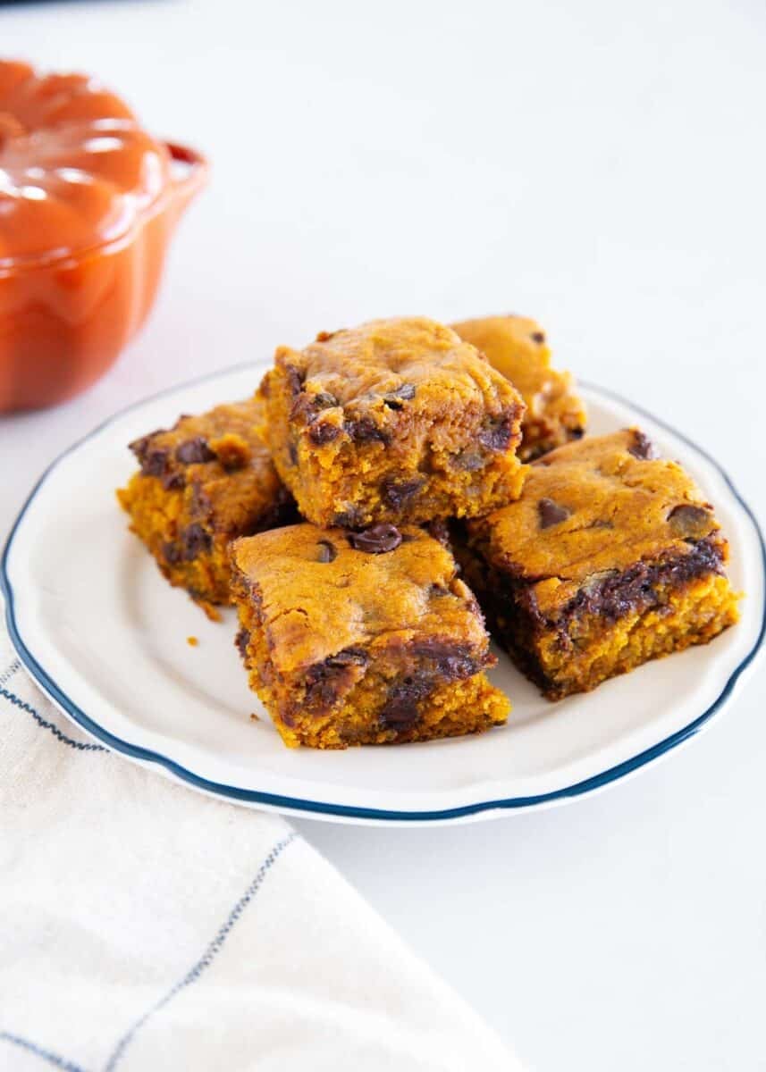 Pumpkin chocolate chip cake squares stacked on a white plate with melted chocolate chips throughout.