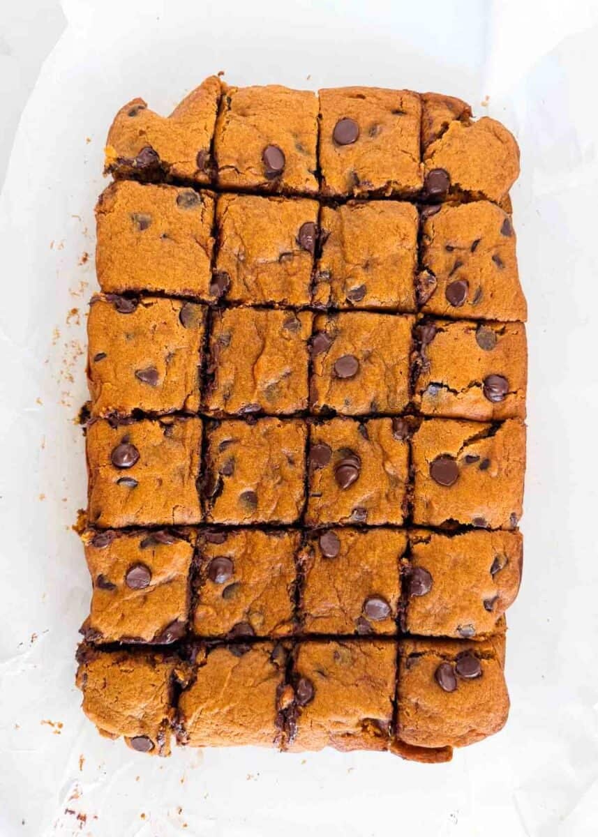 Overhead view of pumpkin chocolate chip cake cut into squares in a parchment-lined pan.