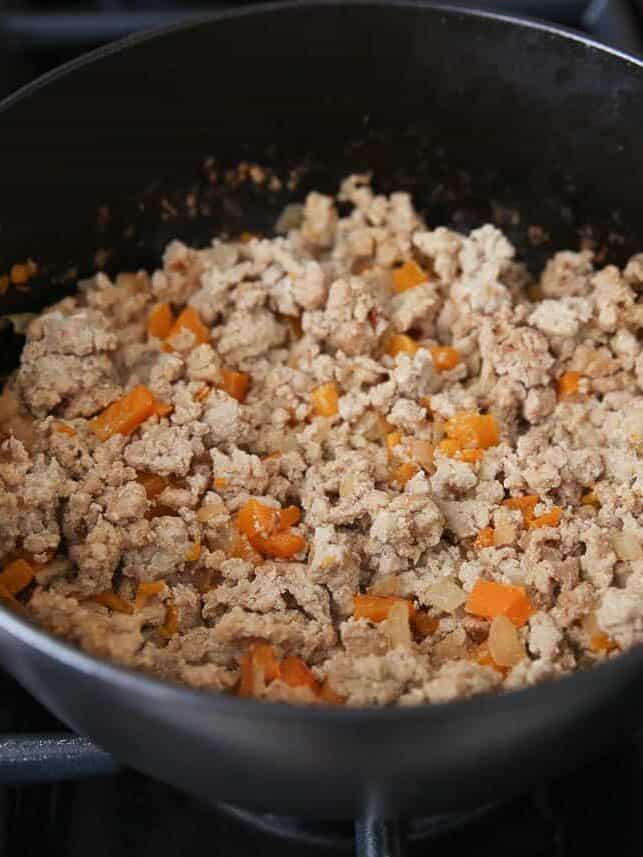Ground turkey cooking with diced onion and bell pepper in a large pot.