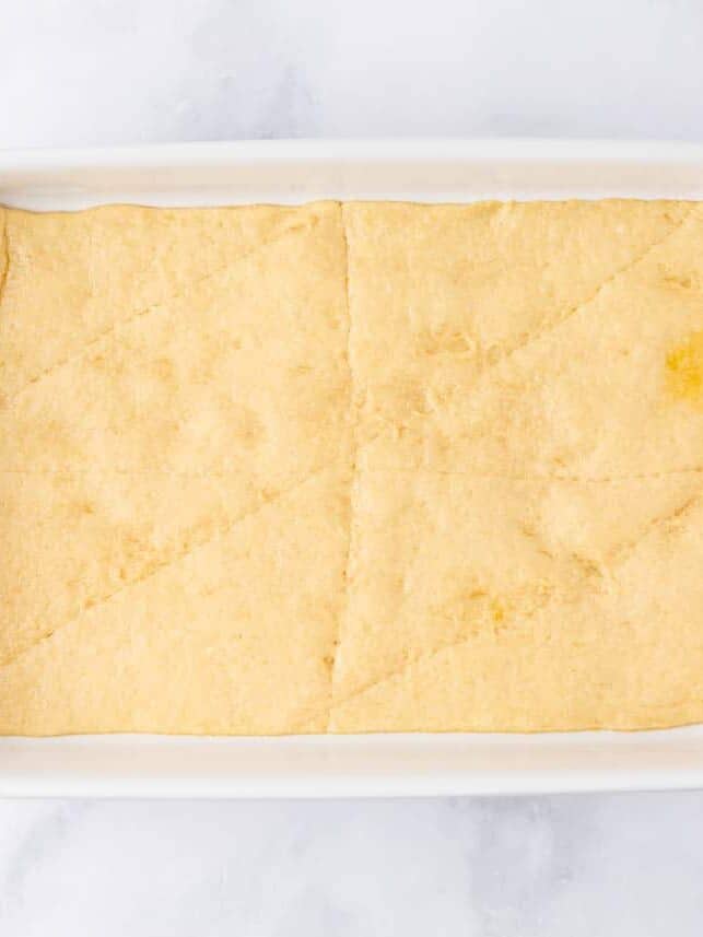 Pressing crescent dough into white baking dish.