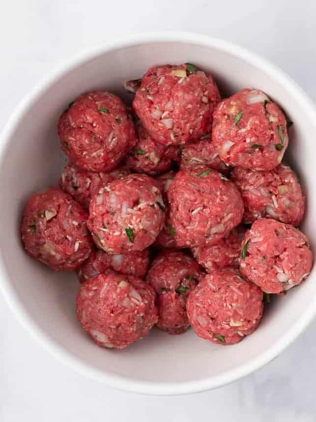 Formed raw porcupine meatballs in a white bowl.