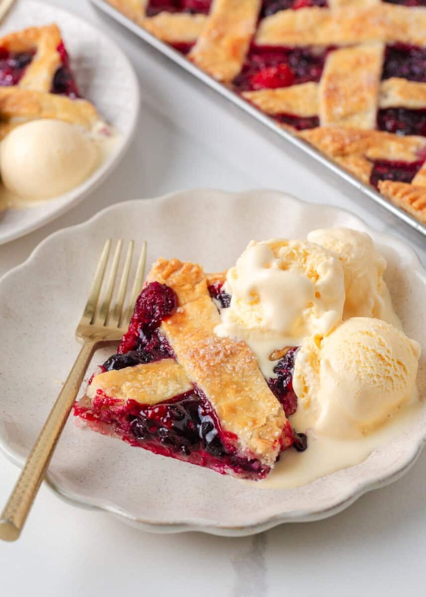 Slice of mixed berry sheet pan pie served warm with vanilla ice cream.