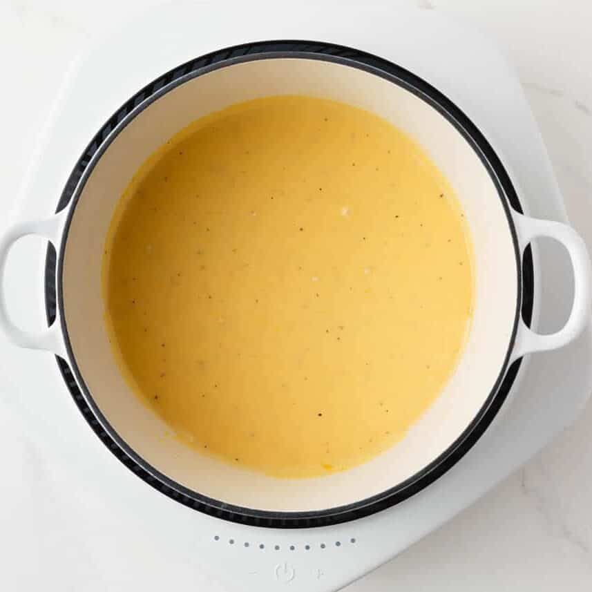 Cheese sauce for potatoes au gratin cooking in a white saucepan, made with melted cheddar cheese and seasonings.