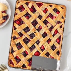 Overhead view of mixed berry sheet pan pie with a lattice crust and one slice removed.