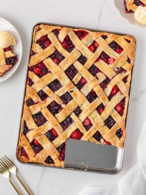 Overhead view of mixed berry sheet pan pie with a lattice crust and one slice removed.