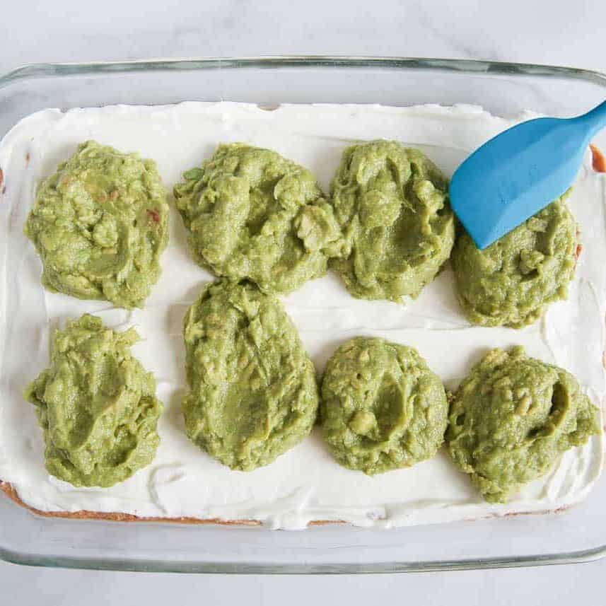 Spreading guacamole over a sour cream layer in 7 layer dip.