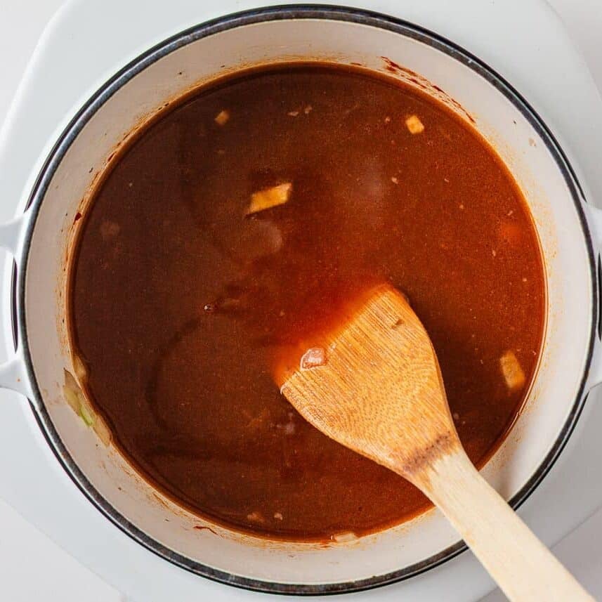 Beef stew broth simmering in a Dutch oven with a wooden spoon.