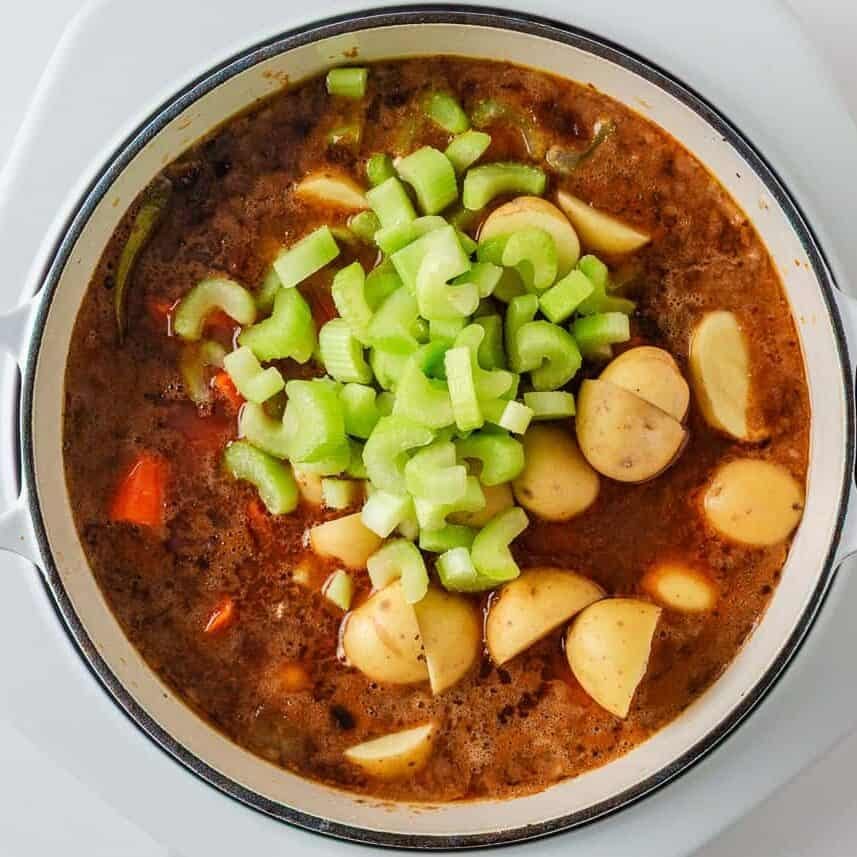 Potatoes and chopped celery added to Dutch oven beef stew as it simmers.