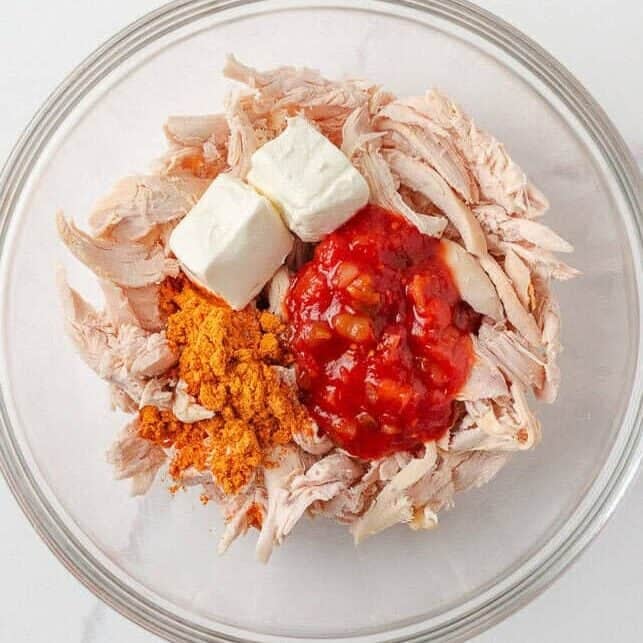 Shredded chicken, cream cheese, salsa and taco seasoning in a glass mixing bowl.