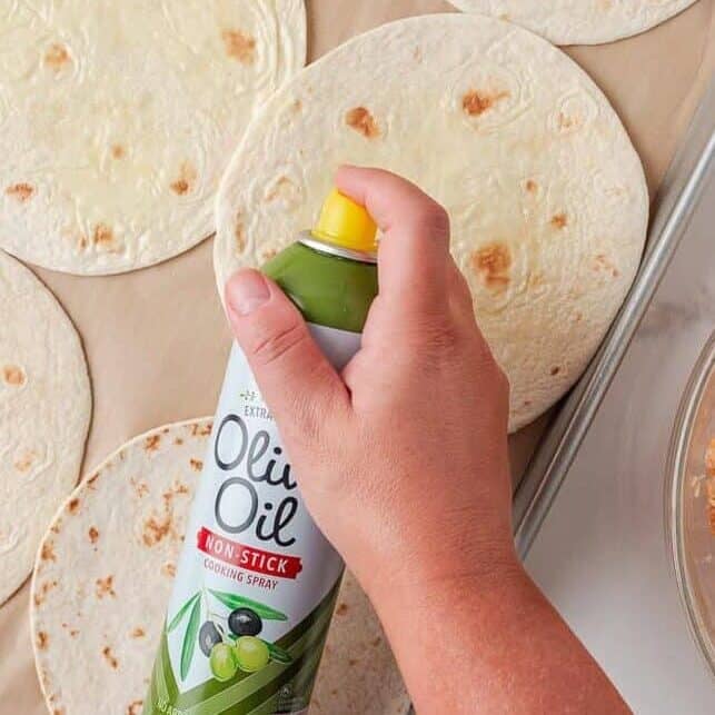 Flour tortillas sprayed with cooking oil on a baking sheet beside the chicken filling.
