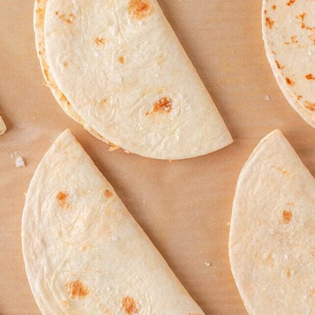 Folded chicken tacos arranged on a parchment-lined baking sheet before baking.