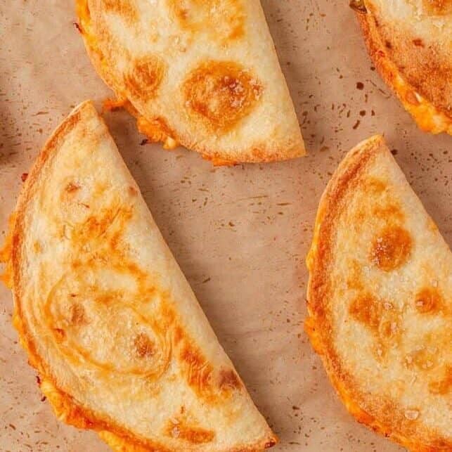 Freshly baked crispy chicken tacos arranged on a parchment-lined baking sheet.
