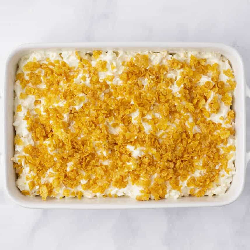 Unbaked funeral potatoes recipe with cornflake topping in a white baking dish.