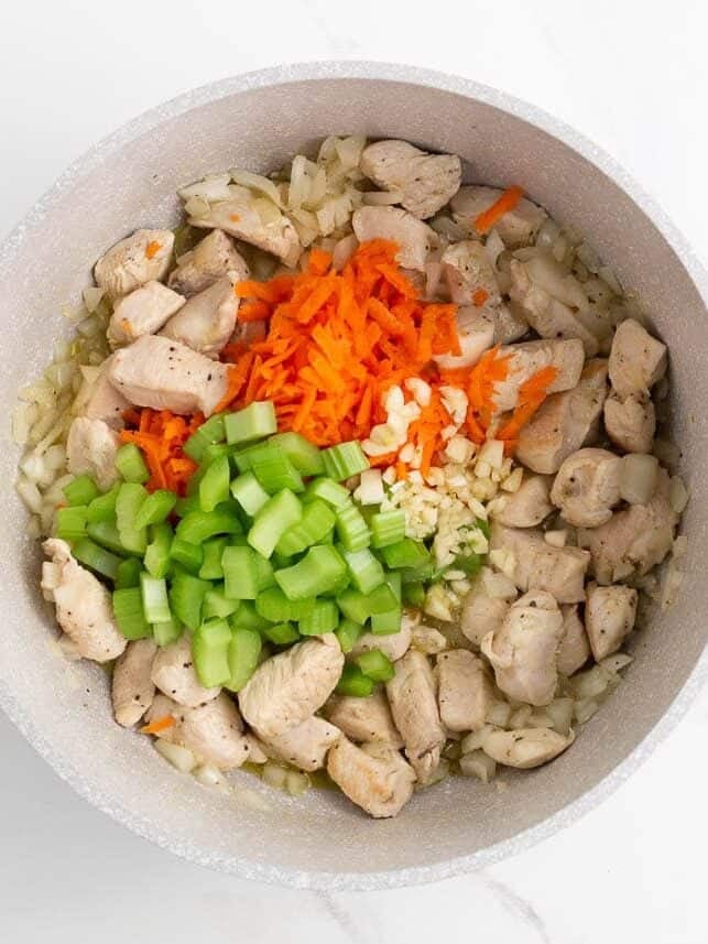 Diced onion, celery, shredded carrot, and garlic added to the pot with cooked chicken.