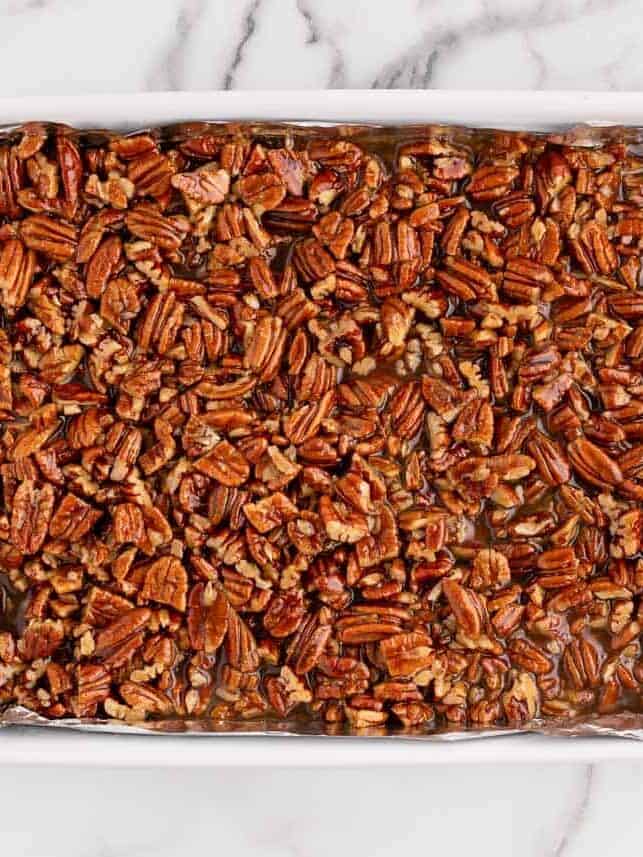Baked pecan pie bars with a shortbread crust in baking dish on counter.