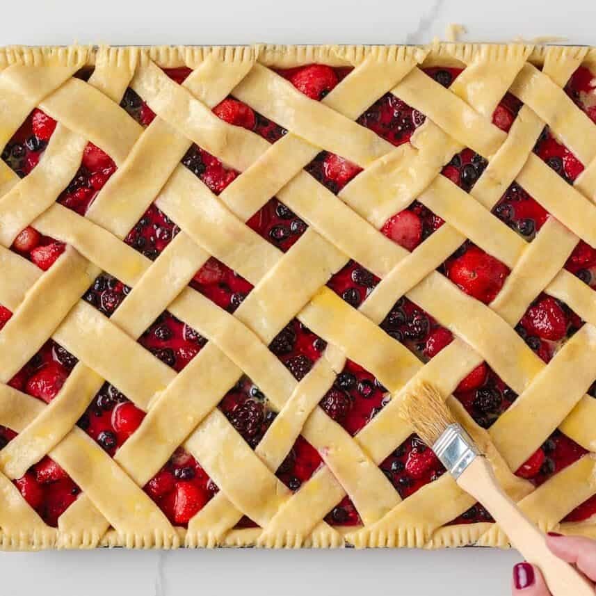 Unbaked berry slab pie topped with lattice crust and brushed with egg wash.