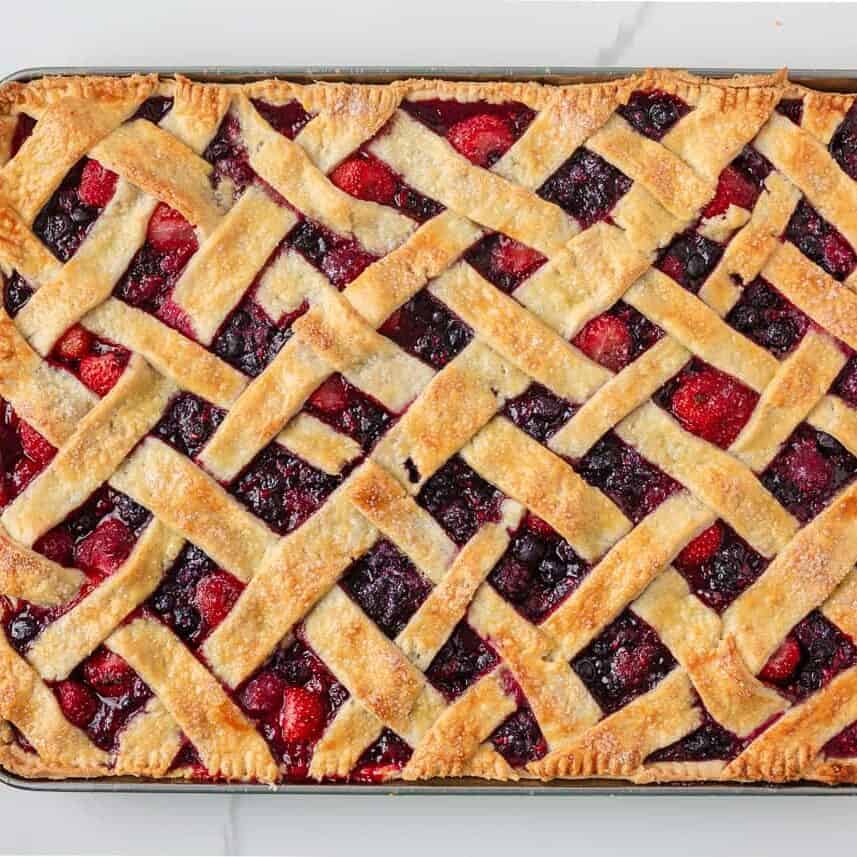 Baked mixed berry sheet pan pie with golden lattice crust on a baking sheet.