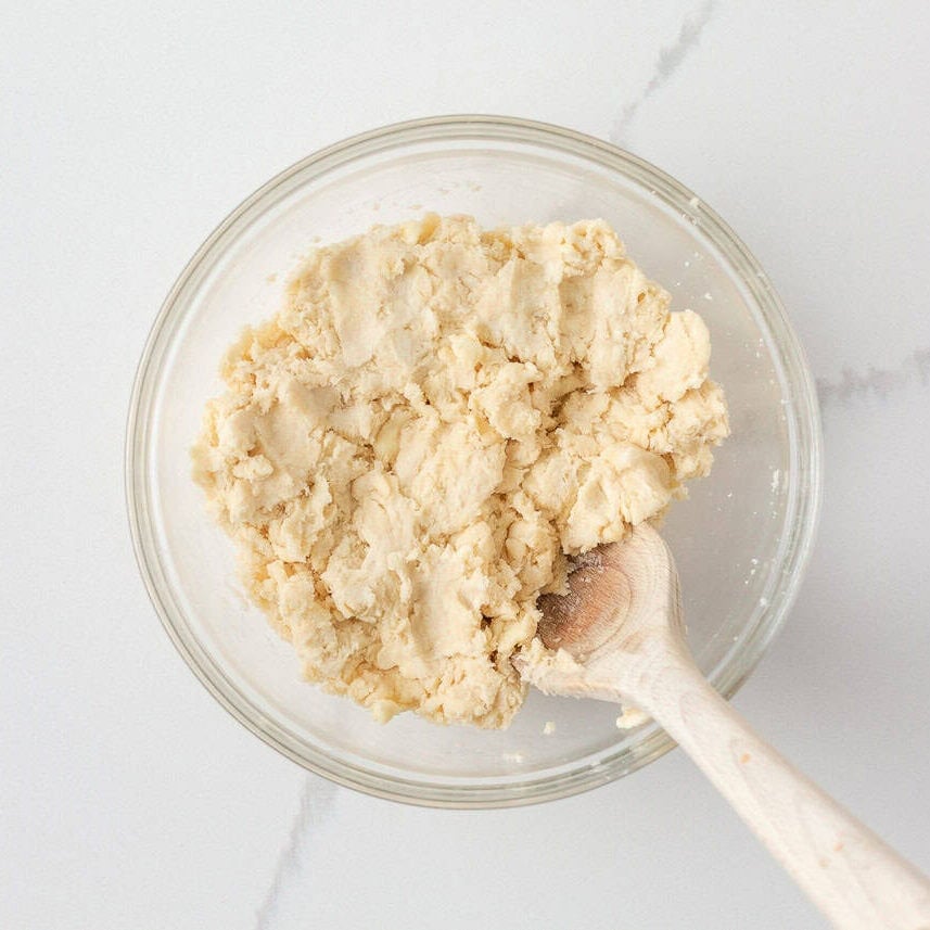 Homemade pie dough mixed in a glass bowl with a wooden spoon.