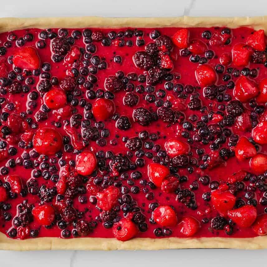 Mixed berry filling spread over pie crust in a sheet pan before adding the lattice topping.