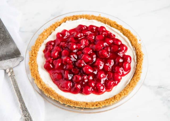 This no-bake cheesecake recipe is perfect for beginners! Only 5 ingredients and absolutely no baking. It's everything a cheesecake should be...silky, smooth, light, creamy and decadent! no bake cheesecake in pan with cherry filling on top