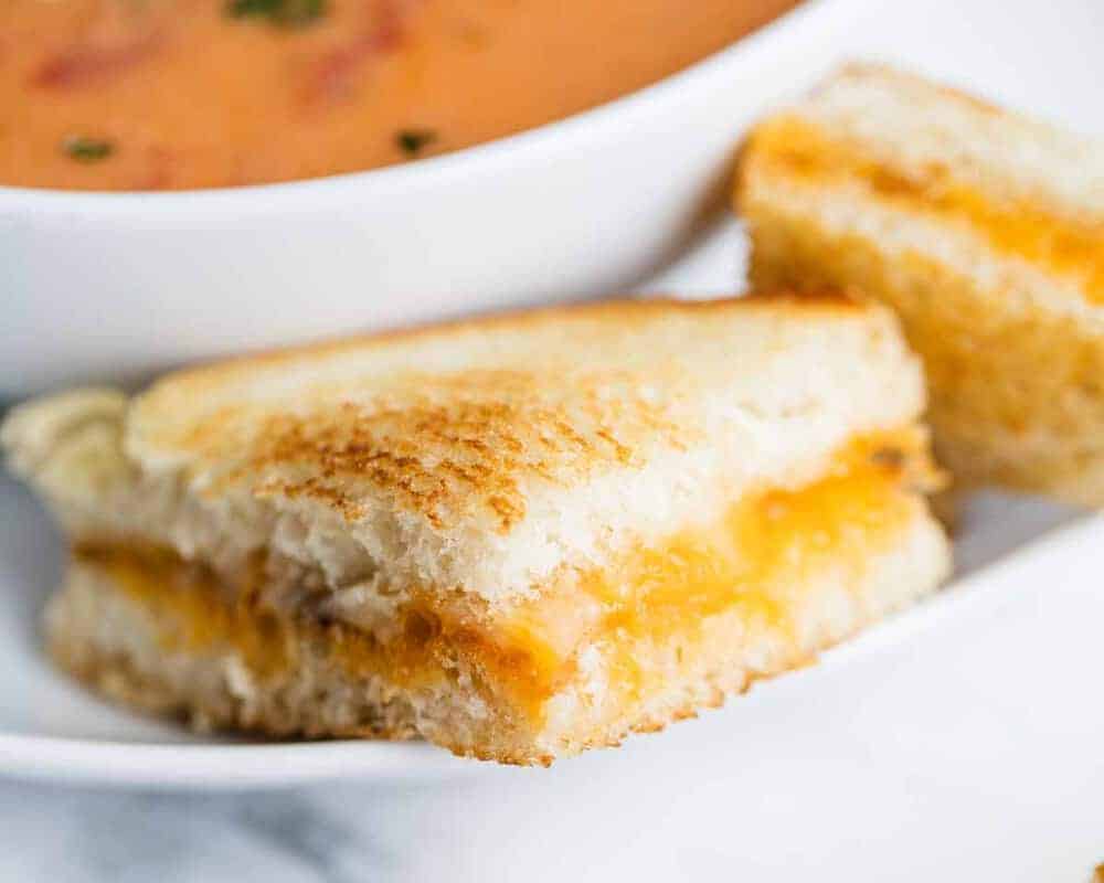 Sliced grilled cheese sandwich on a plate with tomato soup.