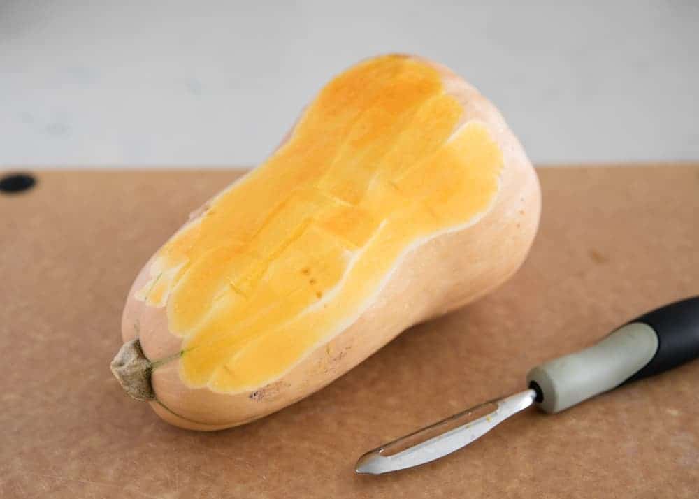 Peeling a butternut squash with a potato peeler.