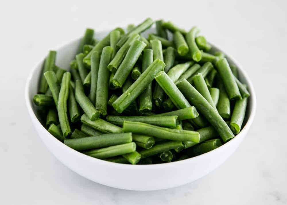 Raw green beans in a white bowl.